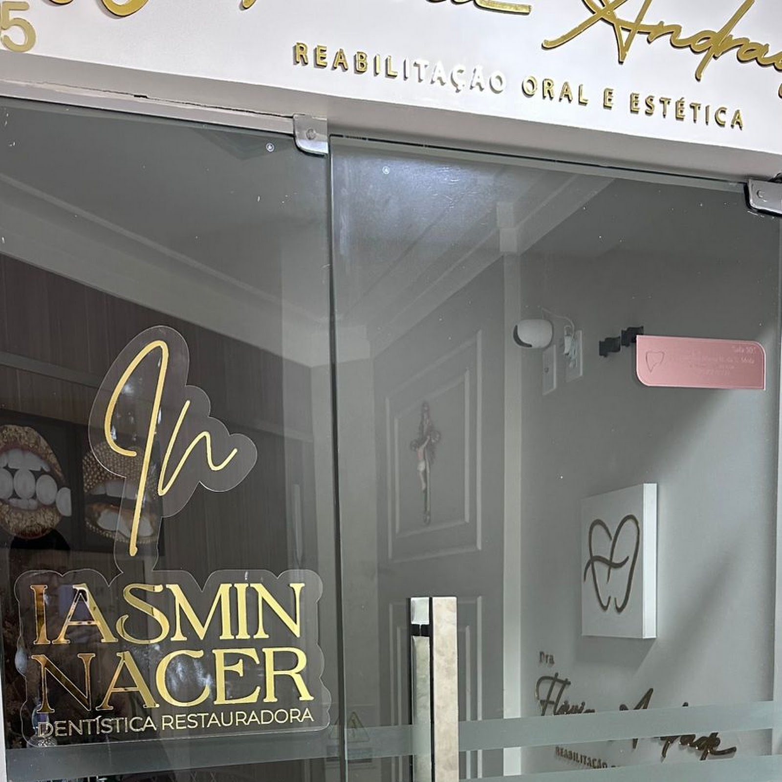 O vidro da porta da clínica com o monograma 'In' em traço único dourado e o nome Iasmin Nacer / Dentística Restauradora.