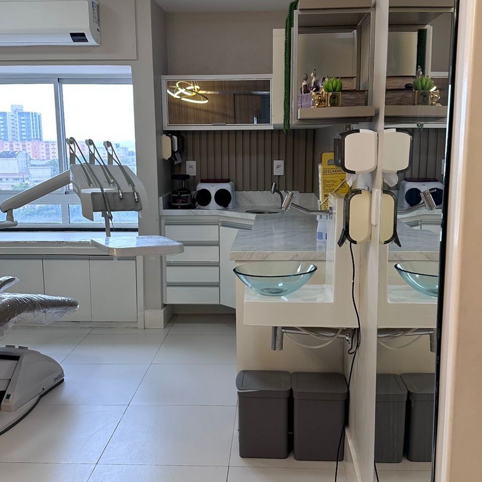 A sala de atendimento da clínica em Aracaju, cadeira odontológica, bancada e janela com a cidade ao fundo.